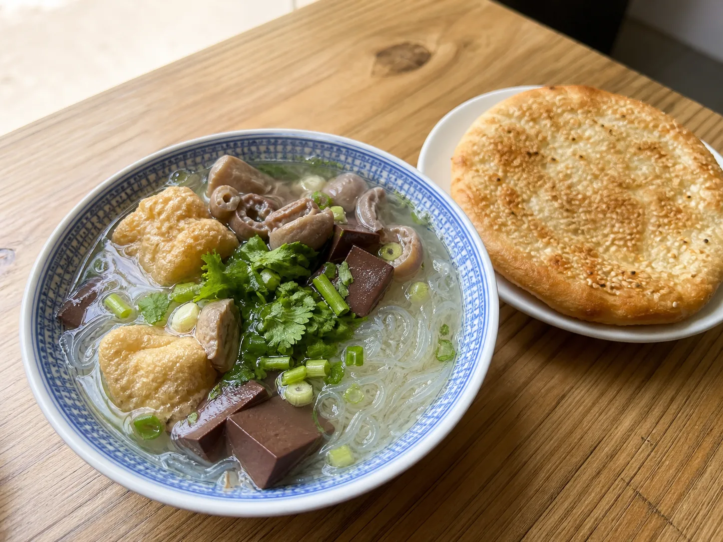 AI-generated editorial image of Nanjing duck-blood vermicelli soup with a sesame flatbread