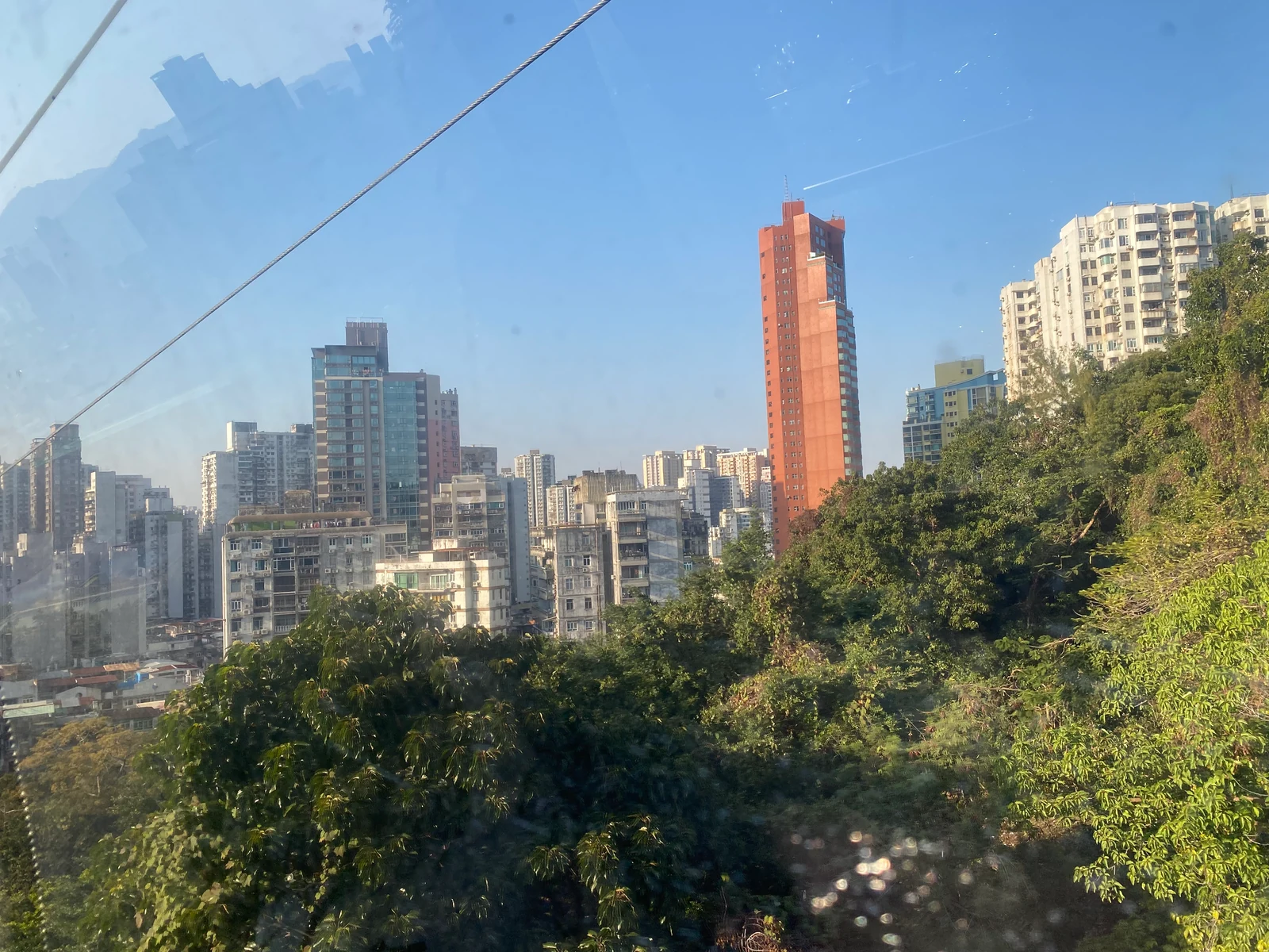 Macau residential skyline and green hillside seen through the Guia Hill cable-car window