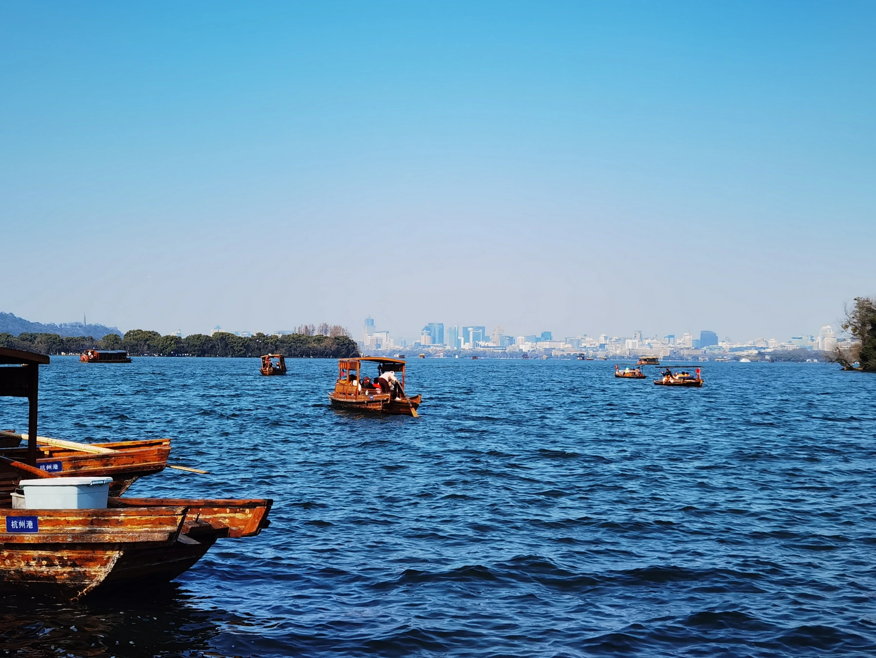 Passenger boats on West Lake with open water and distant city buildings